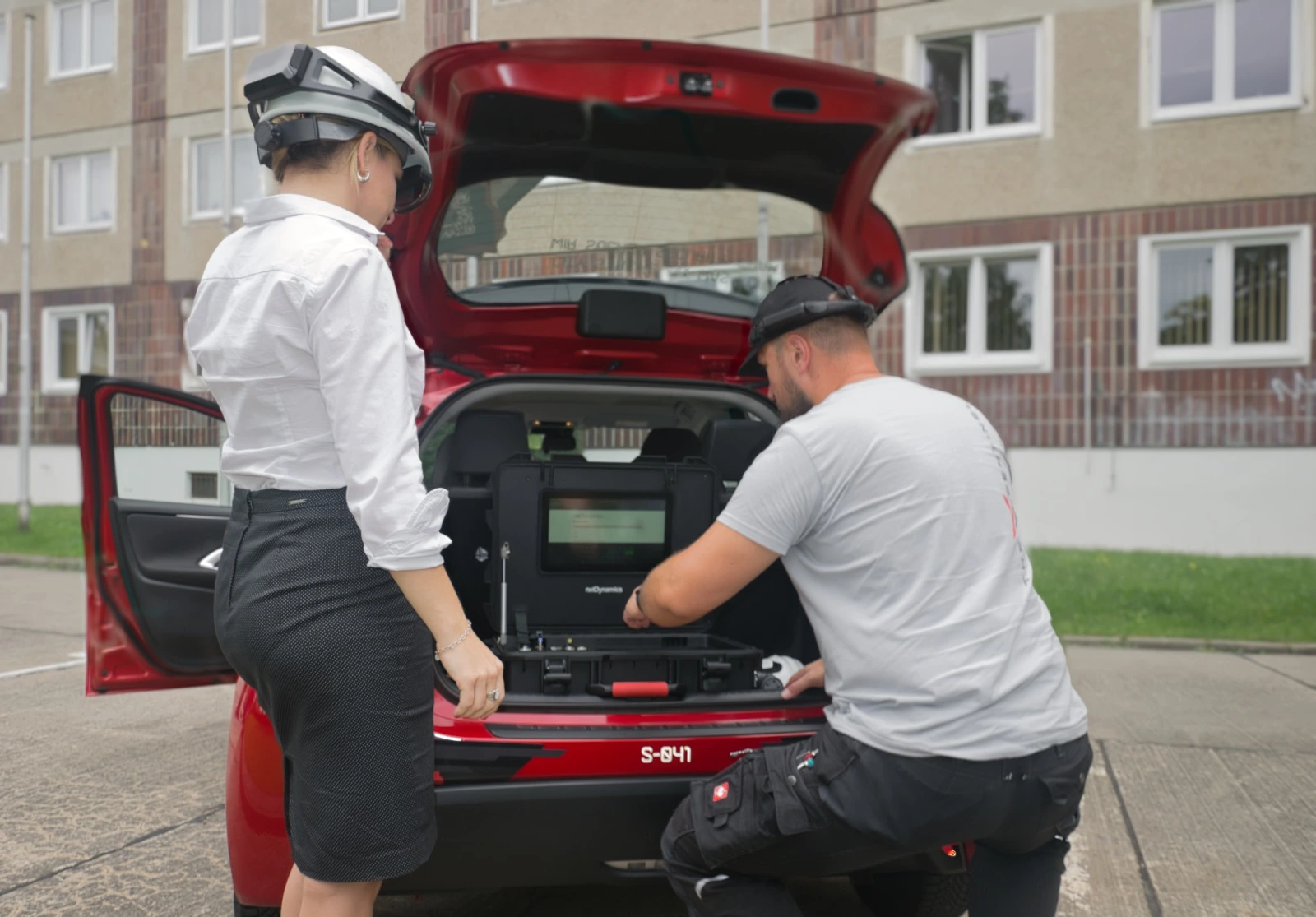 Mann und Frau mit tragbaren Brillensystemen am Auto und mobiler Kofferplattform